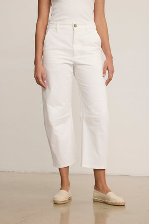 A person wearing a sleeveless white top, Velvet by Graham & Spencer ALEXIS PANT in white cotton twill with knee darting, and beige espadrille shoes stands against a plain background.