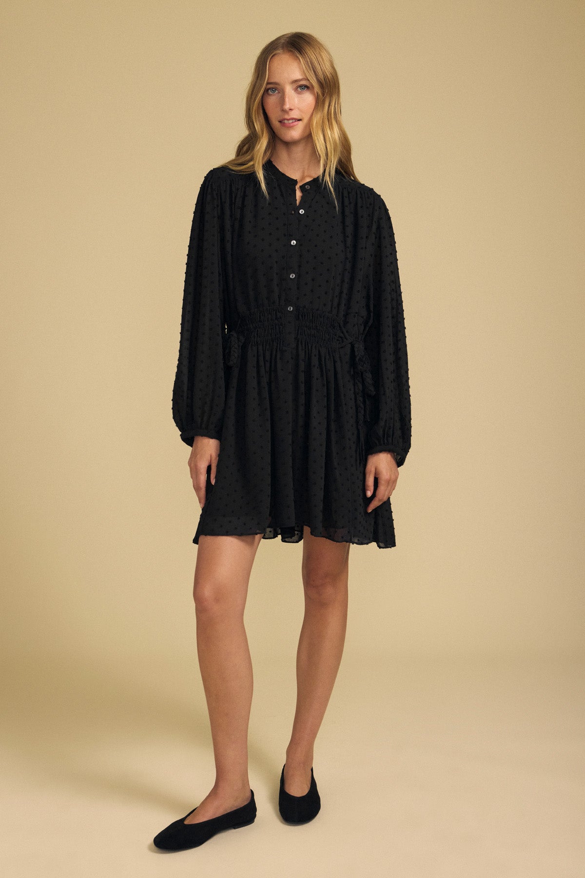 A person wearing a black Velvet by Graham & Spencer BRINLEY TEXTURED CREPE DRESS featuring a button-down front, gathered waist, and long sleeves, paired with black ballet flats.-46488137040065