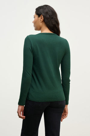 A woman faces away, wearing the LIZZIE TEE by Velvet by Graham & Spencer—a long sleeve cotton slub tee with a crew neckline—and black pants, set against a plain light background.