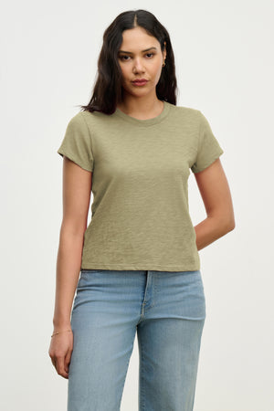 A woman with long dark hair wears the MARIE TEE by Velvet by Graham & Spencer in olive green, paired with light blue jeans, posing against a plain light background.