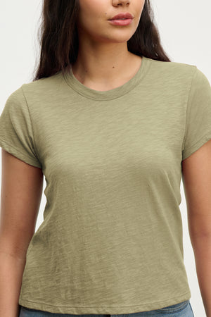 A woman wears the MARIE TEE by Velvet by Graham & Spencer, a light olive green cotton slub casual top with a relaxed boxy fit, standing against a plain background.
