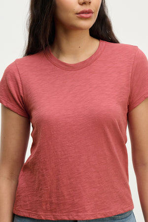 A woman wears the MARIE TEE by Velvet by Graham & Spencer—a relaxed, boxy-fit short-sleeve cotton slub t-shirt in faded red—against a plain light background, ideal for casual occasions.