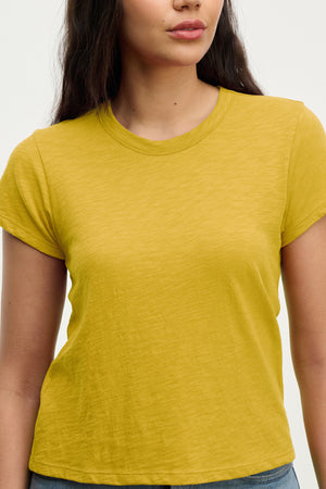 A woman wears the MARIE TEE by Velvet by Graham & Spencer—a short-sleeved yellow cotton slub t-shirt with a relaxed boxy fit—paired with blue jeans, standing against a plain light background for a casual look.