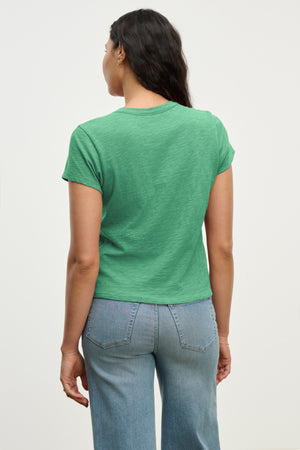 A person faces away, wearing the MARIE TEE by Velvet by Graham & Spencer—a green cotton slub short-sleeve with a relaxed boxy fit—and light blue jeans, set against a plain light background.