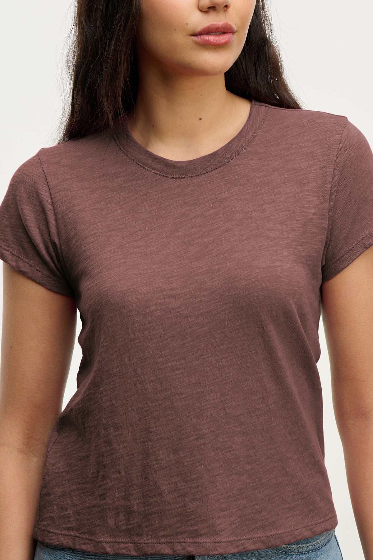 A woman wears the MARIE TEE by Velvet by Graham & Spencer, a short-sleeved brown cotton slub crew neck, standing against a plain light background.