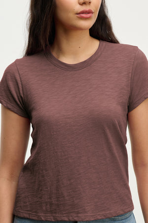 A woman wears the MARIE TEE by Velvet by Graham & Spencer, a short-sleeved brown cotton slub crew neck, standing against a plain light background.