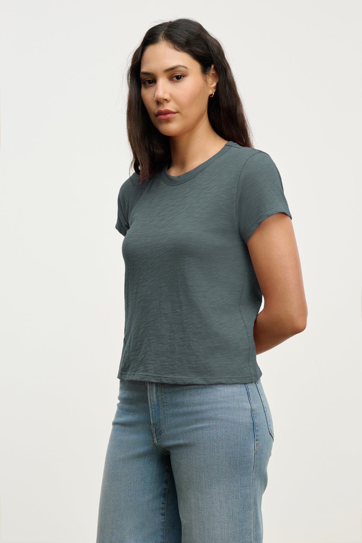 A woman with long dark hair models the MARIE TEE by Velvet by Graham & Spencer, a short-sleeved gray cotton slub top, paired with light blue jeans—an effortless choice for any casual occasion.-39319760765121
