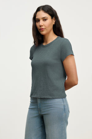 A woman with long dark hair models the MARIE TEE by Velvet by Graham & Spencer, a short-sleeved gray cotton slub top, paired with light blue jeans—an effortless choice for any casual occasion.