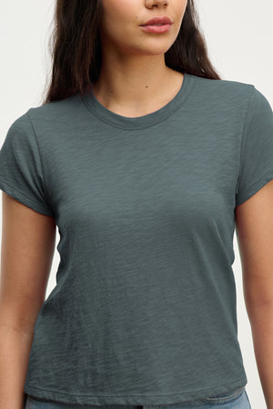 A woman wears the MARIE TEE by Velvet by Graham & Spencer, a short-sleeved, dark gray cotton slub t-shirt with a relaxed boxy fit, shown from shoulders to waist against a plain background.