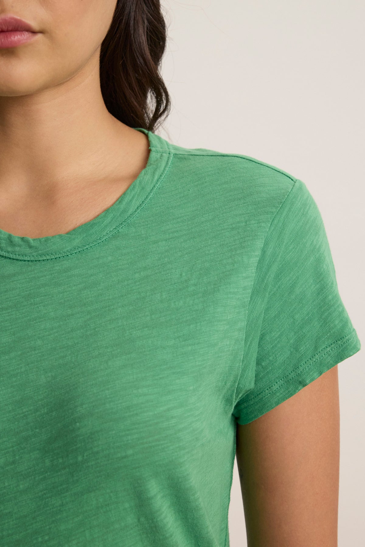 A person models the SIA T-SHIRT DRESS by Velvet by Graham & Spencer—a green, crew neck, mini-length dress in textured cotton slub—showing only the lower half of their face, neck, and upper torso.