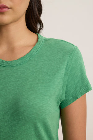 A person models the SIA T-SHIRT DRESS by Velvet by Graham & Spencer—a green, crew neck, mini-length dress in textured cotton slub—showing only the lower half of their face, neck, and upper torso.
