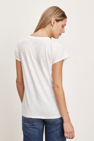 A person with long blonde hair, wearing a plain white JILIAN TEE by Velvet by Graham & Spencer made from cotton slub fabric and blue jeans, is seen from behind, looking downward.