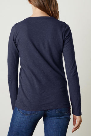 Rear view of a person with long hair wearing a navy blue LIZZIE TEE by Velvet by Graham & Spencer and blue jeans, standing against a plain white background.