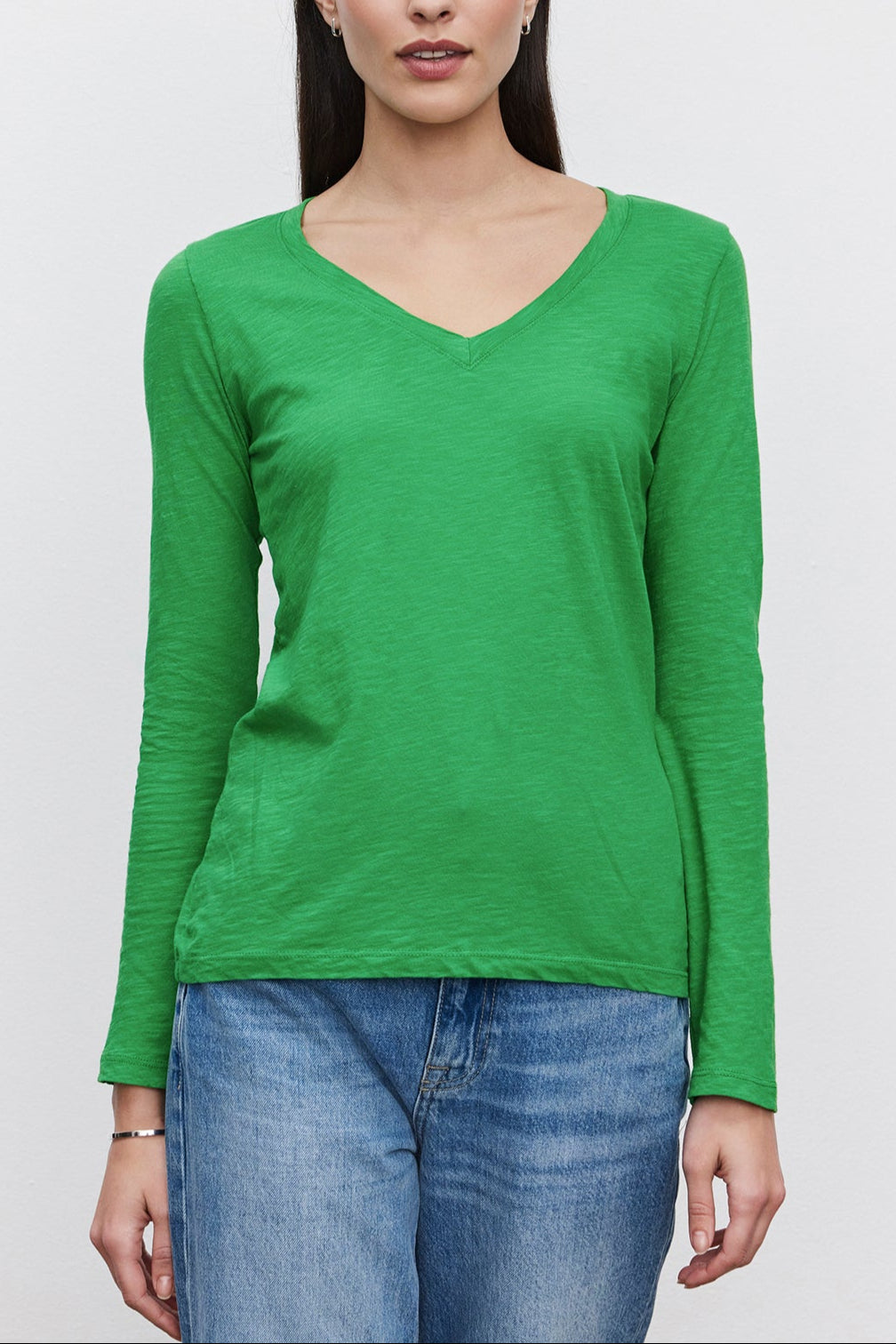 A woman with long dark hair wearing a green BLAIRE TEE by Velvet by Graham & Spencer and blue jeans stands against a plain white background.-36201431138497