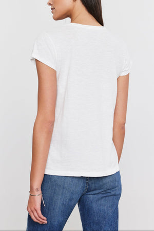 A person with long hair, wearing a white Velvet by Graham & Spencer KIRA TEE with a scoop neckline and blue jeans, is shown from the back against a plain white background.