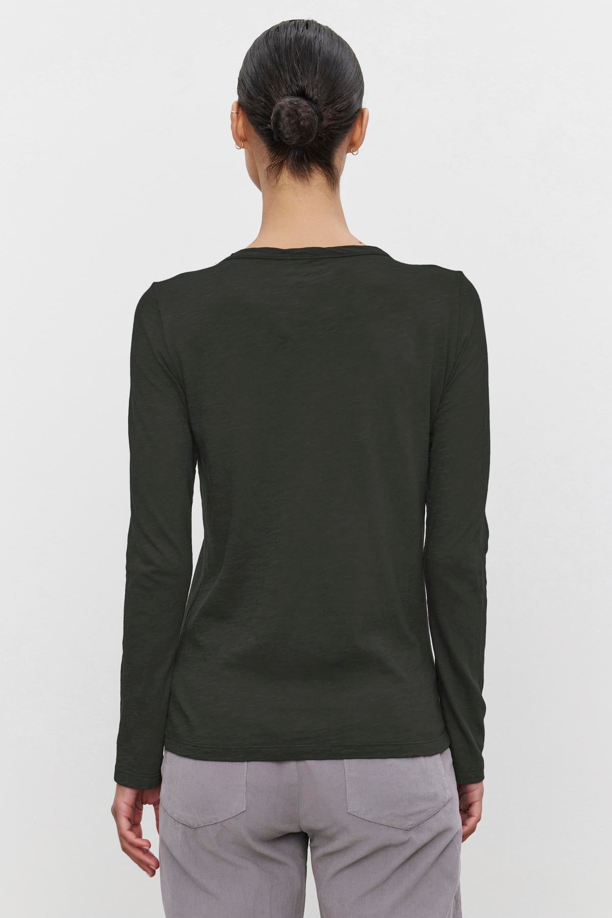 Someone with their hair in a bun is wearing the LIZZIE TEE, a long-sleeved dark green shirt by Velvet by Graham & Spencer, crafted from textured cotton slub. They are also wearing light gray pants, and the view is from behind.
