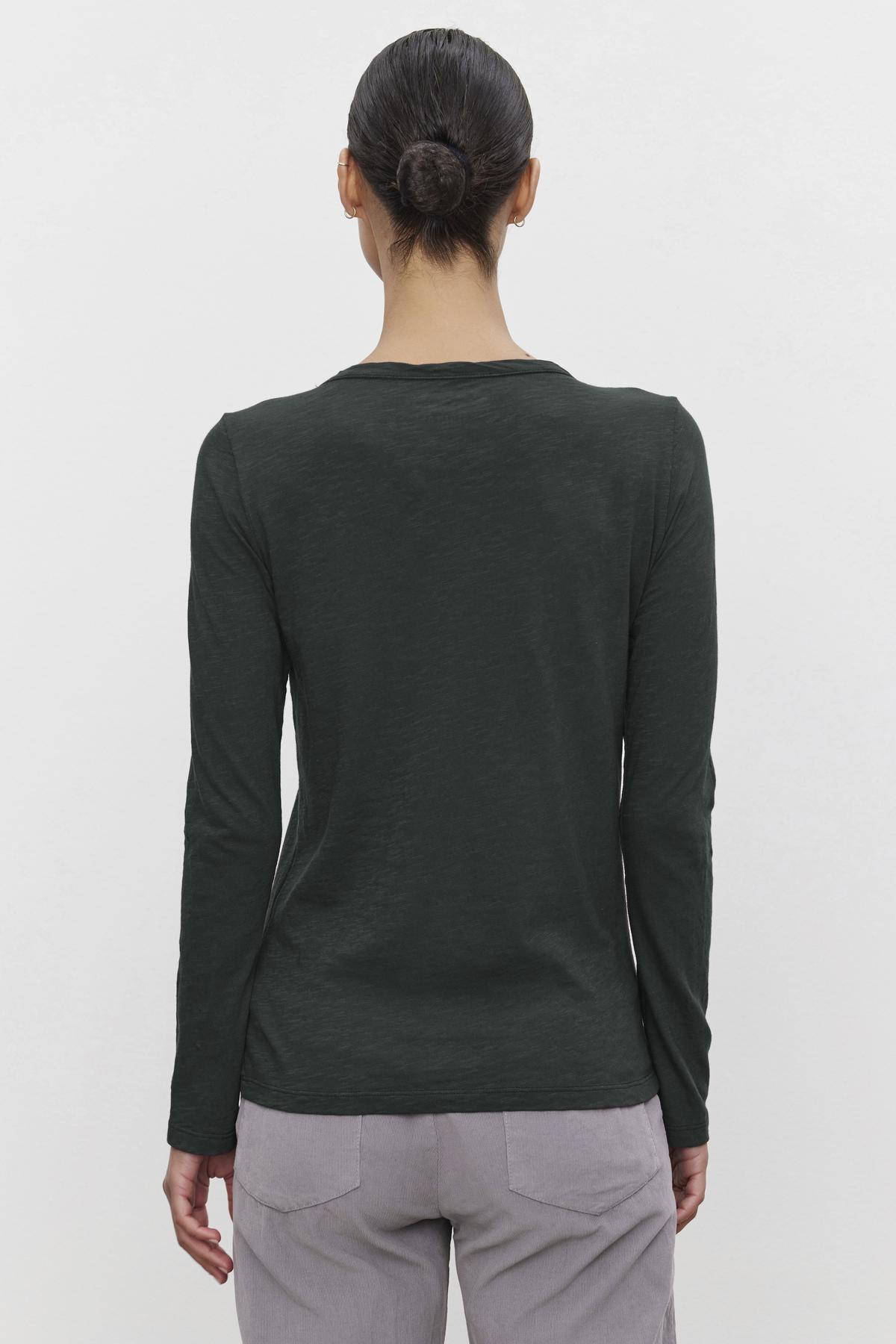A person with dark hair in a bun wears the LIZZIE TEE by Velvet by Graham & Spencer, a long-sleeved dark green shirt crafted from cotton slub, along with light gray pants, facing away.-38139494531265