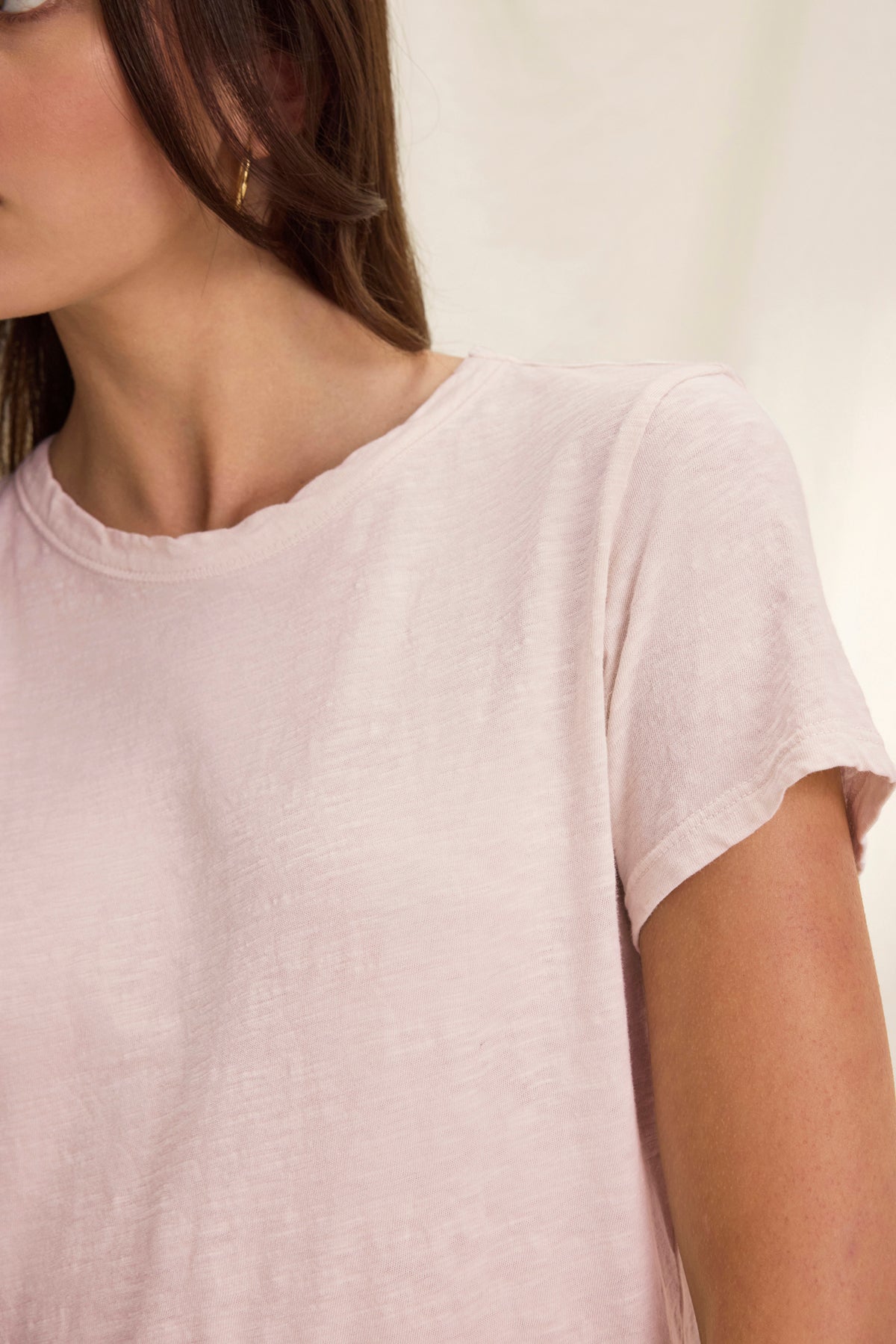 A woman wears the MARIE TEE by Velvet by Graham & Spencer—a light pink cotton slub short-sleeve tee with a relaxed boxy fit and crew neckline—paired with gold hoop earrings, shown from the shoulders up against a neutral background.-39319763222721