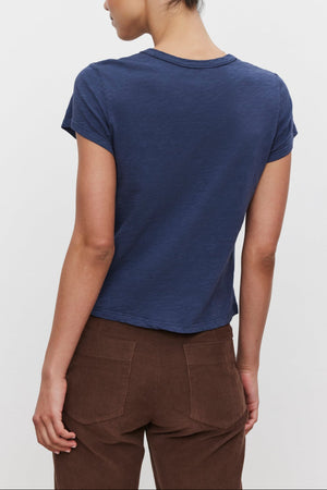 A person with short dark hair is shown from the back wearing the MARIE TEE by Velvet by Graham & Spencer, a navy blue cotton slub t-shirt with a boxy fit, paired with brown pants, making for a perfect casual look.