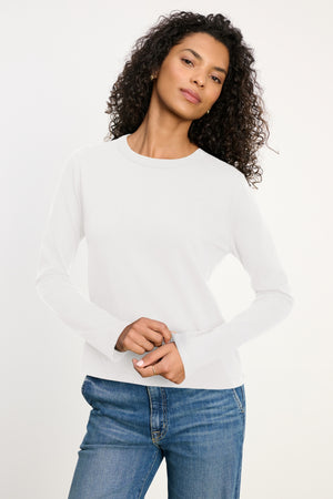 Wearing the SUSANNA TEE by Velvet by Graham & Spencer, a person with curly hair and blue jeans poses against a neutral background.