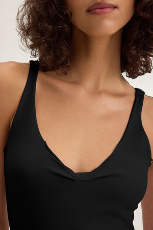 A woman with curly hair models the KIM TANK TOP by Velvet by Graham & Spencer—a black, lightweight cotton sleeveless V-neck, shown from shoulders to just above the lips—making it a versatile wardrobe staple.