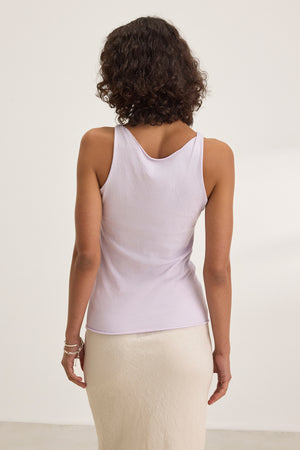 A person with curly hair wears a lightweight KIM TANK TOP by Velvet by Graham & Spencer and a light beige skirt, standing with their back to the camera against a plain background.
