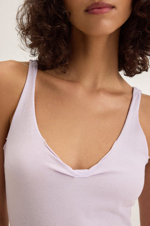 A person with curly hair wears the light purple KIM TANK TOP by Velvet by Graham & Spencer. The image highlights the upper torso and part of the face, showcasing this versatile cotton tank with a scoop neckline.