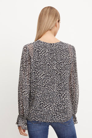 The back view of a woman wearing a Velvet by Graham & Spencer Kathy Printed V-Neck Blouse.