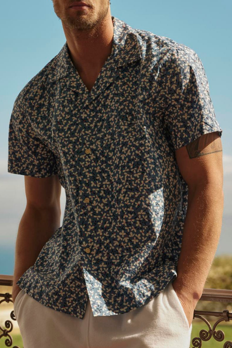 Man in sunglasses and a IGGY BUTTON-UP SHIRT by Velvet by Graham & Spencer standing by a balustrade with a coastal view in the background.