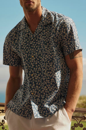 Man in sunglasses and a IGGY BUTTON-UP SHIRT by Velvet by Graham & Spencer standing by a balustrade with a coastal view in the background.