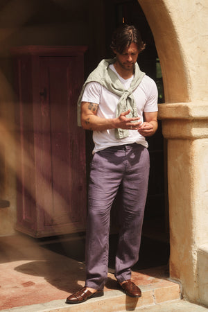 A man stands outside a building wearing a white T-shirt, light green sweater over his shoulders, and Velvet by Graham & Spencer ALFRED LINEN PANT with a rear elastic waistband, looking down at his phone.