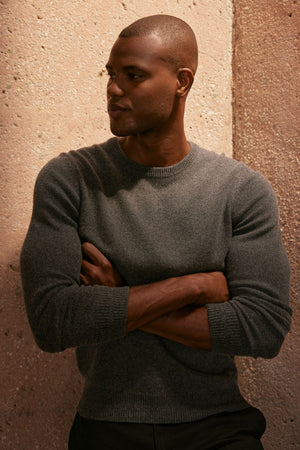 A person in a Velvet by Graham & Spencer DASHELL CREW NECK SWEATER exudes warmth and style as they lean against a wall.