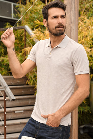 Niko Polo in cobble with dark blue denim, model leaning against wood post outdoors