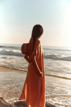 Wearing the MAEVE LINEN DRESS by Velvet by Graham & Spencer, a person stands on the beach gazing at the ocean—a stylish choice for casual seaside outings.
