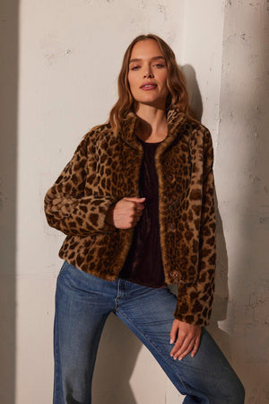A person in a VALLI FAUX FUR JACKET by Velvet by Graham & Spencer and jeans poses against a textured wall.