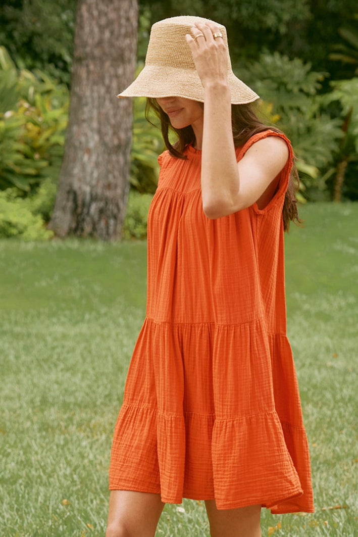 Woman in an airy SUSIE COTTON GAUZE DRESS by Velvet by Graham & Spencer and straw hat walking on a stone path in a garden with lush greenery.