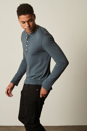 a man wearing a blue Velvet by Graham & Spencer ALVARO COTTON JERSEY HENLEY shirt and black pants.
