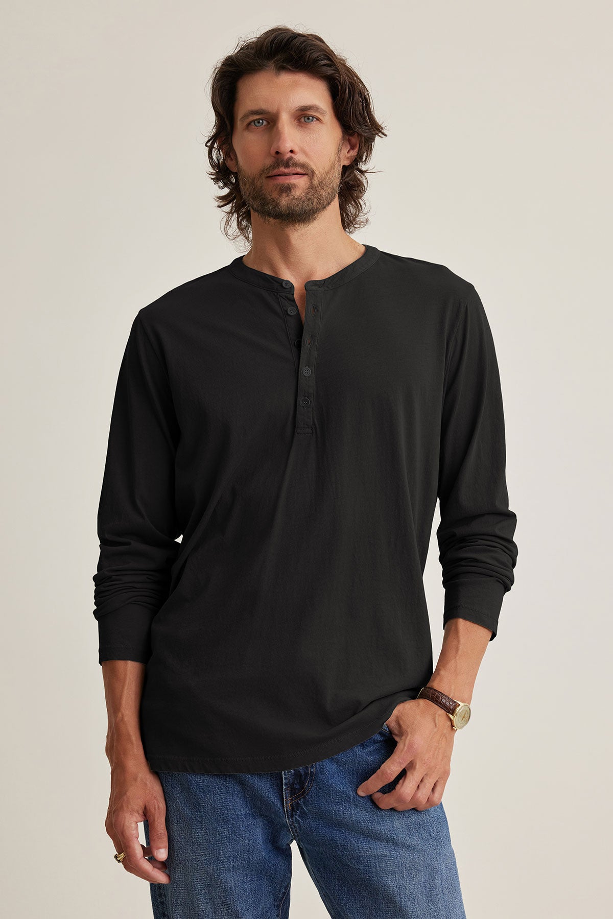 A man with long hair and a beard wears the ALVARO HENLEY by Velvet by Graham & Spencer, along with blue jeans, standing against a plain background, perfect for stylish layering.-39025854644417
