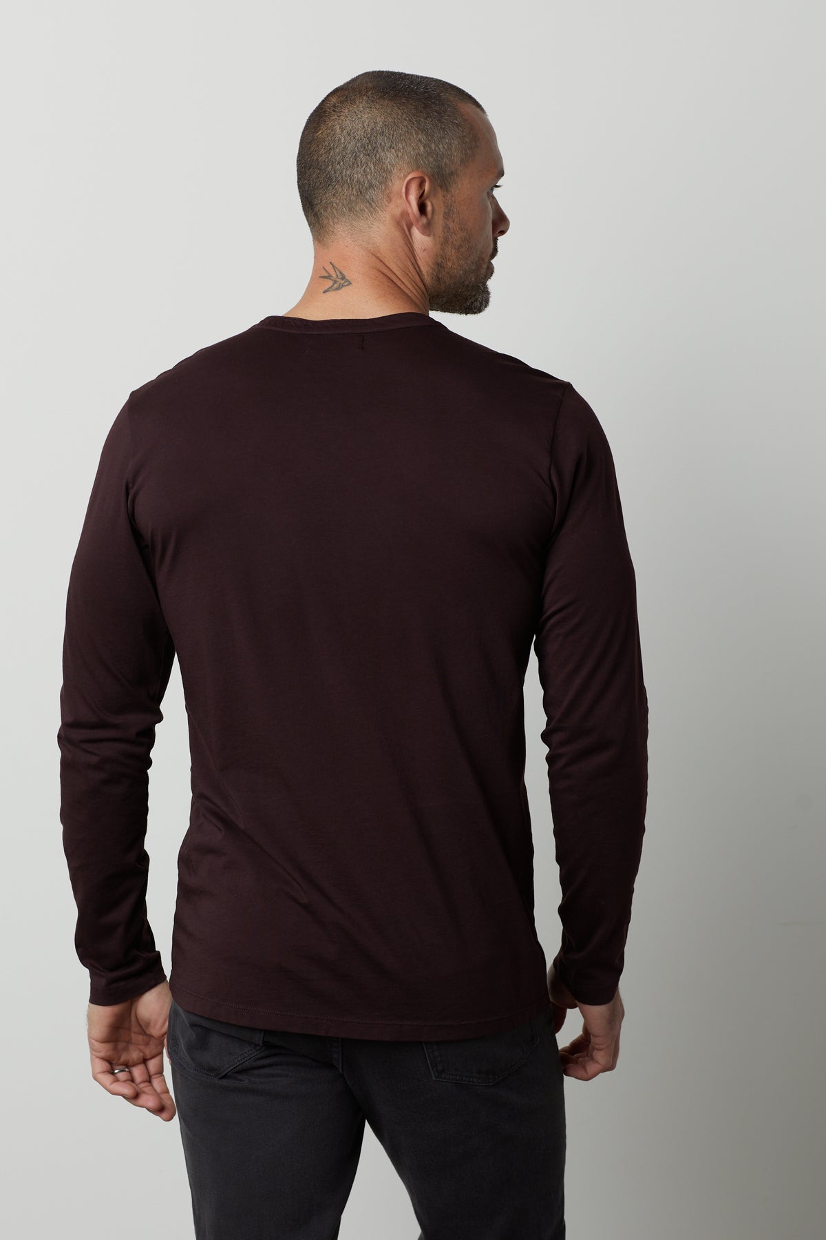 A man with a shaved head and a tattoo on his neck is seen from the back, wearing a dark ALVARO HENLEY by Velvet by Graham & Spencer and dark pants.-35547510407361