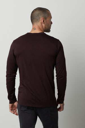 A man with a shaved head and a tattoo on his neck is seen from the back, wearing a dark ALVARO HENLEY by Velvet by Graham & Spencer and dark pants.