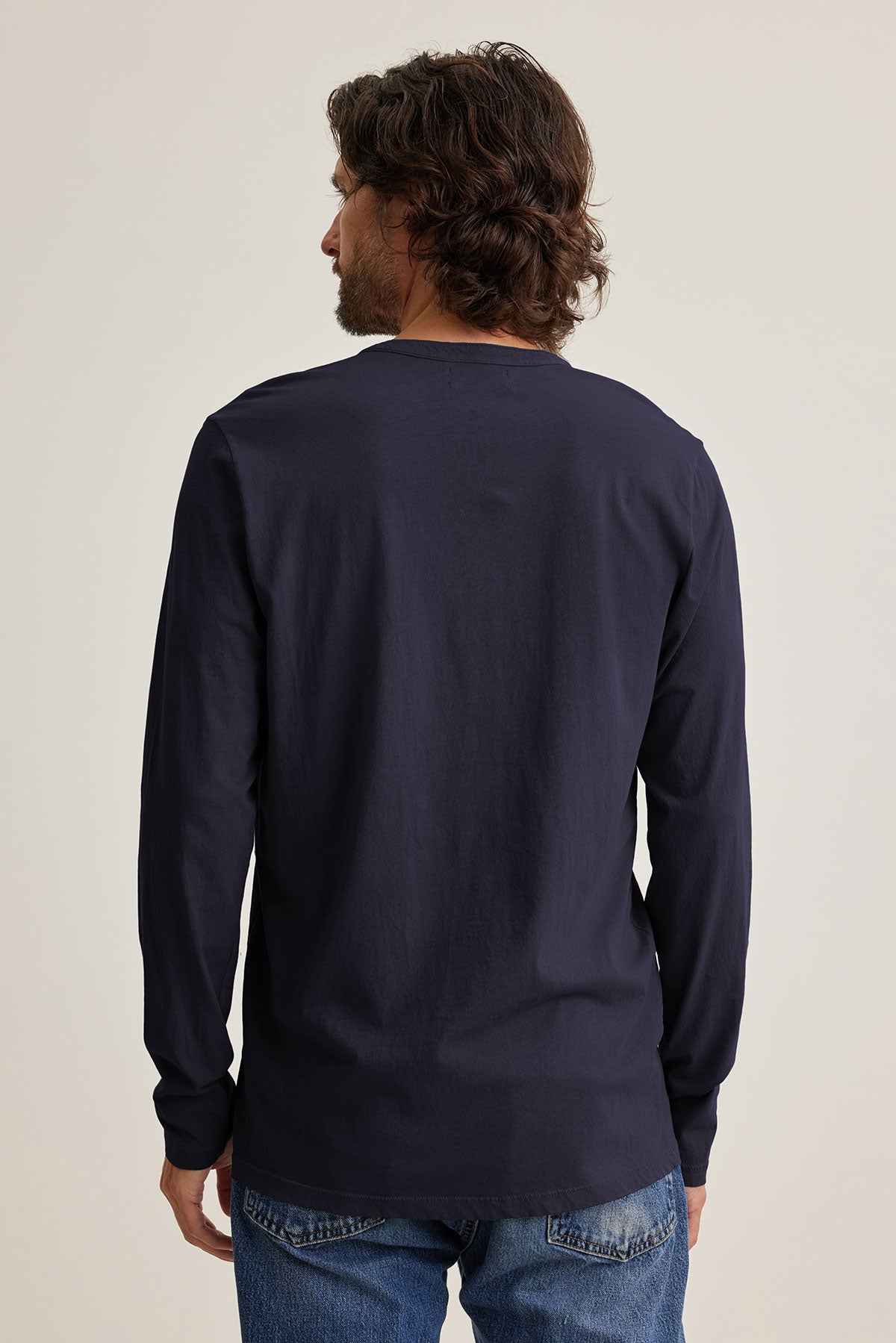 A man with shoulder-length hair faces away, wearing the ALVARO HENLEY by Velvet by Graham & Spencer over his jeans.-39025854906561