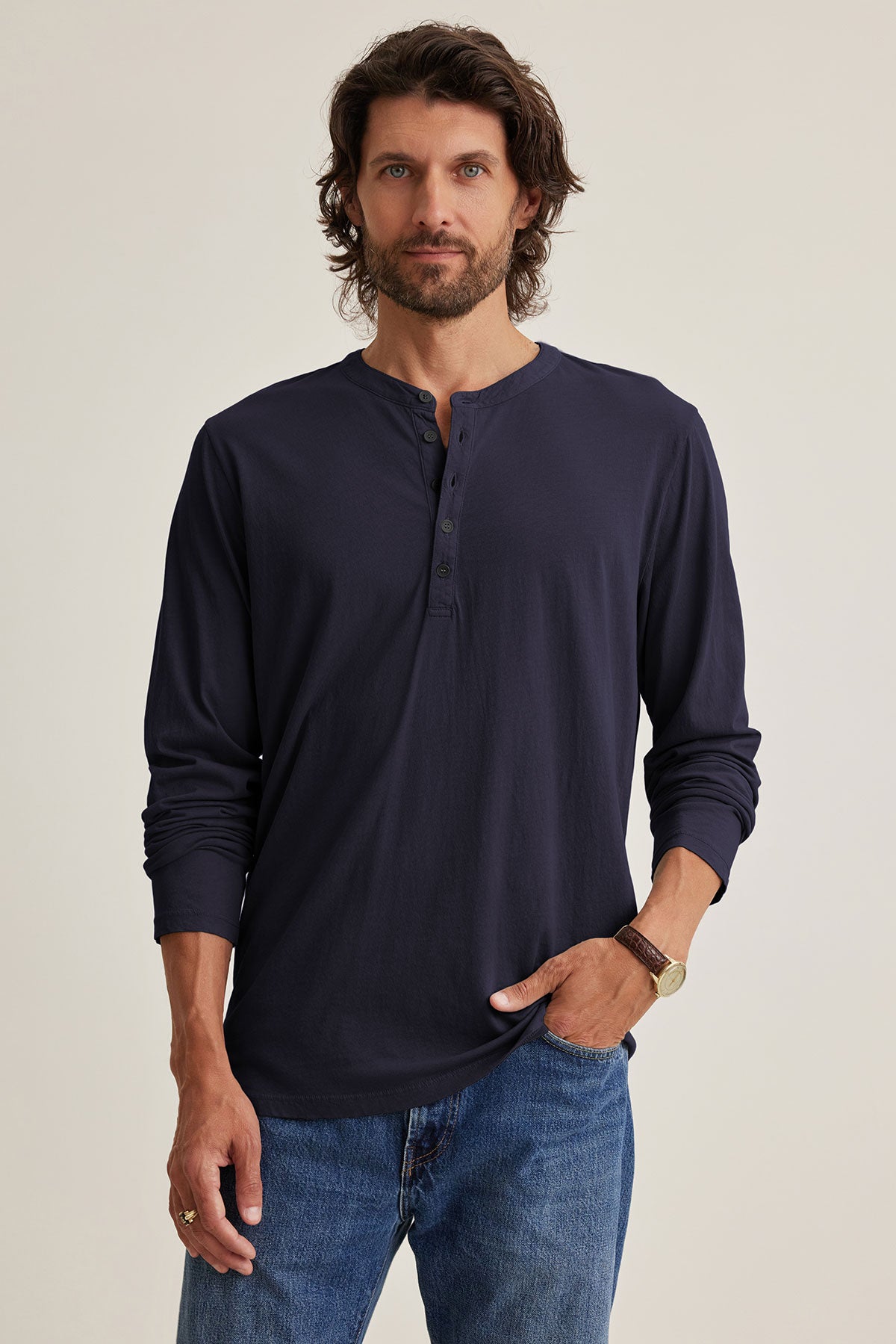 A man with long hair and a beard wears the navy ALVARO HENLEY by Velvet by Graham & Spencer, perfectly layered over jeans against a neutral background.-39025854841025
