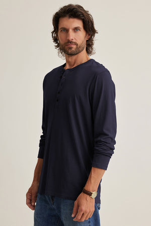 A man with wavy hair is wearing the ALVARO HENLEY by Velvet by Graham & Spencer and jeans.