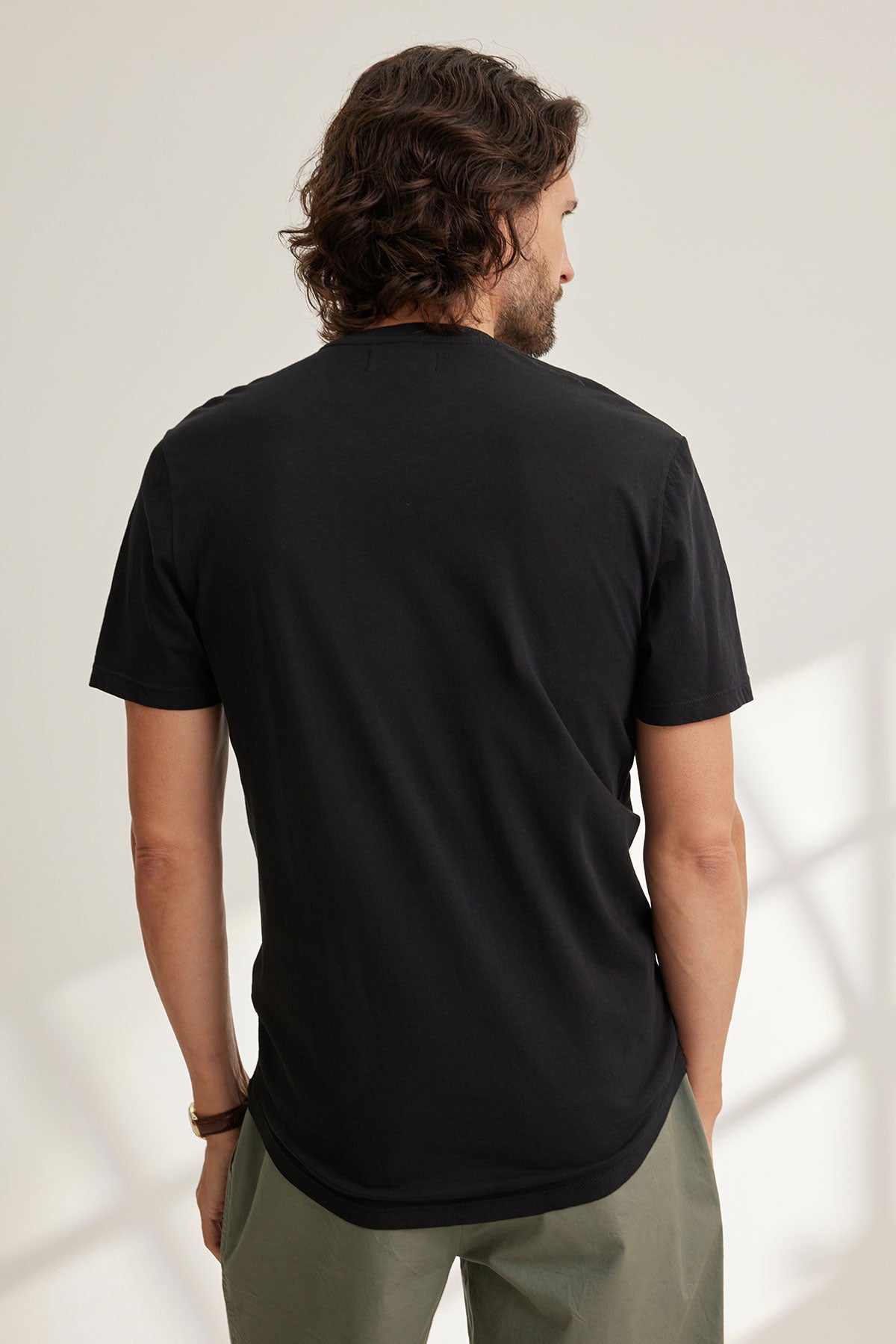 A person with long hair is seen from behind wearing Velvet by Graham & Spencer's Fulton Henley in black and green pants, standing in a well-lit room.