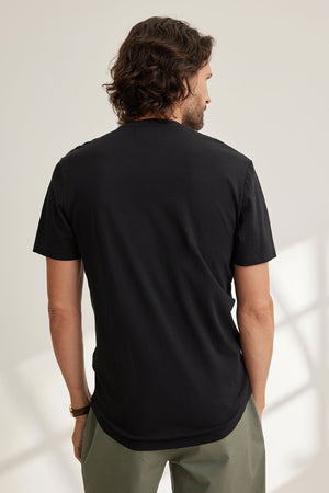 A person with long hair is seen from behind wearing Velvet by Graham & Spencer's Fulton Henley in black and green pants, standing in a well-lit room.