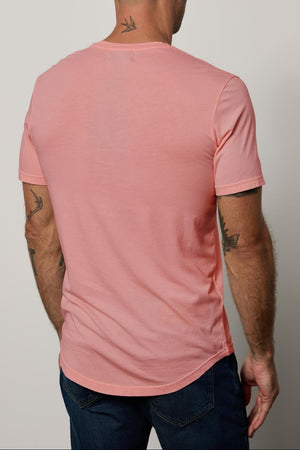 A man with tattoos on his neck and arms, wearing 004 Clear sunglasses by Chimi, a pink t-shirt, and blue jeans, is standing with his back to the camera against a plain background.