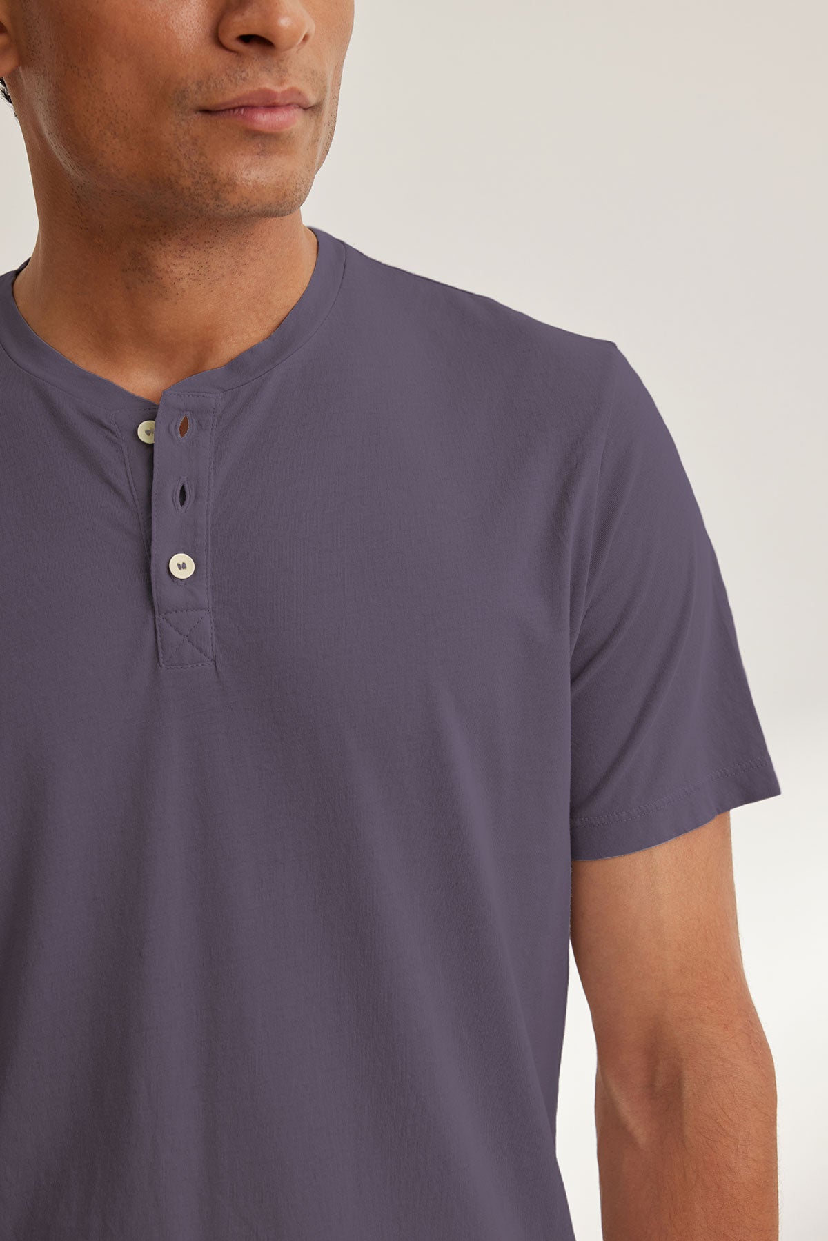 Wearing the FULTON HENLEY by Velvet by Graham & Spencer, a person stands against a neutral backdrop in a soft gray Pima jersey henley tee with buttons. Only the upper torso and part of their face are visible.-38670204829889