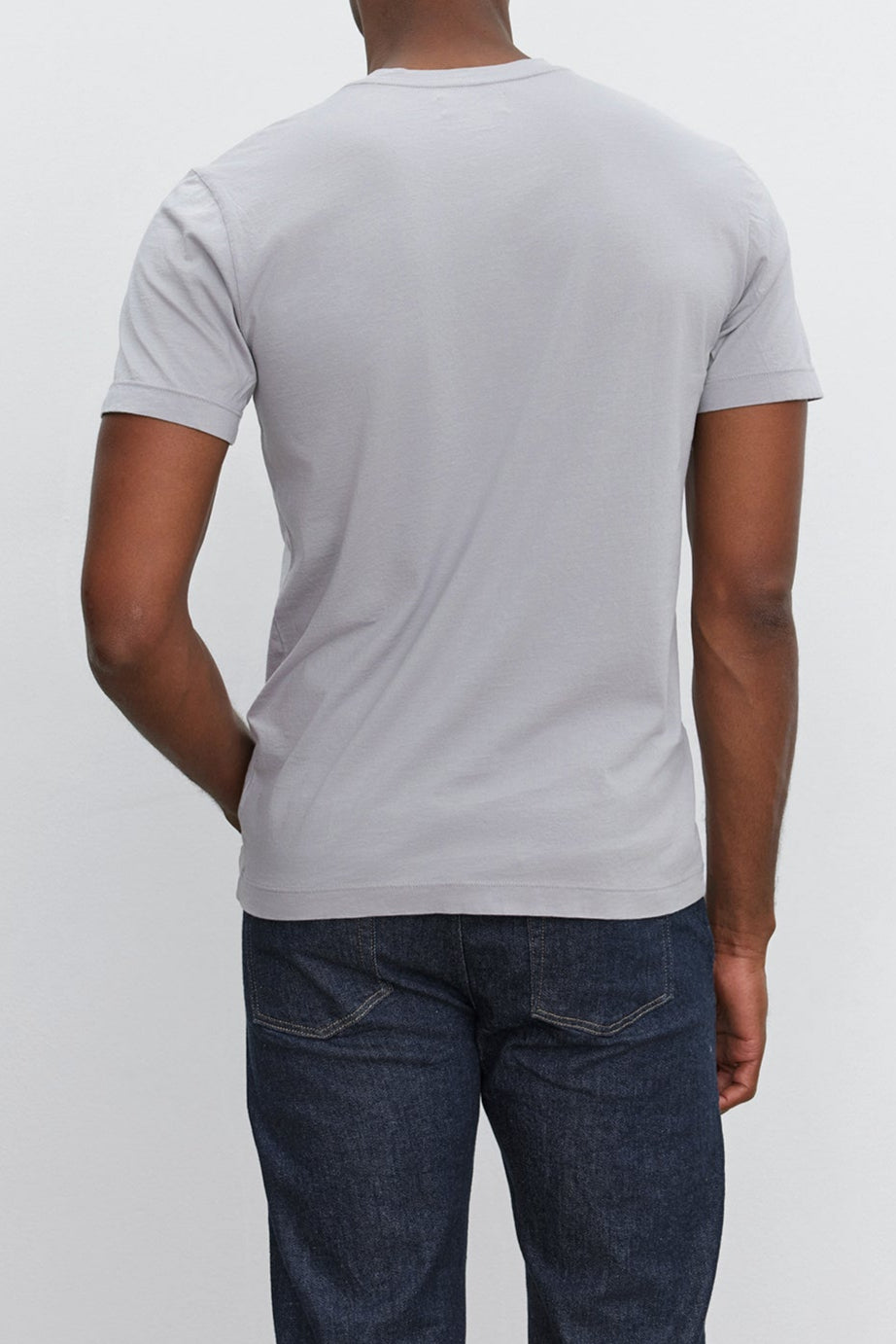 Back view of a person wearing the HOWARD TEE by Velvet by Graham & Spencer, a lightweight cotton knit light gray short-sleeve t-shirt, and dark blue jeans against a plain white background.-37386166206657