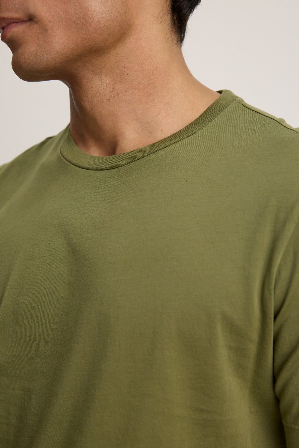 A close-up of a person wearing the HOWARD TEE by Velvet by Graham & Spencer in olive green Pima jersey, highlighting the neckline, shoulder, and part of the face and neck.-39446027862209