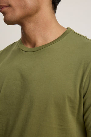 A close-up of a person wearing the HOWARD TEE by Velvet by Graham & Spencer in olive green Pima jersey, highlighting the neckline, shoulder, and part of the face and neck.
